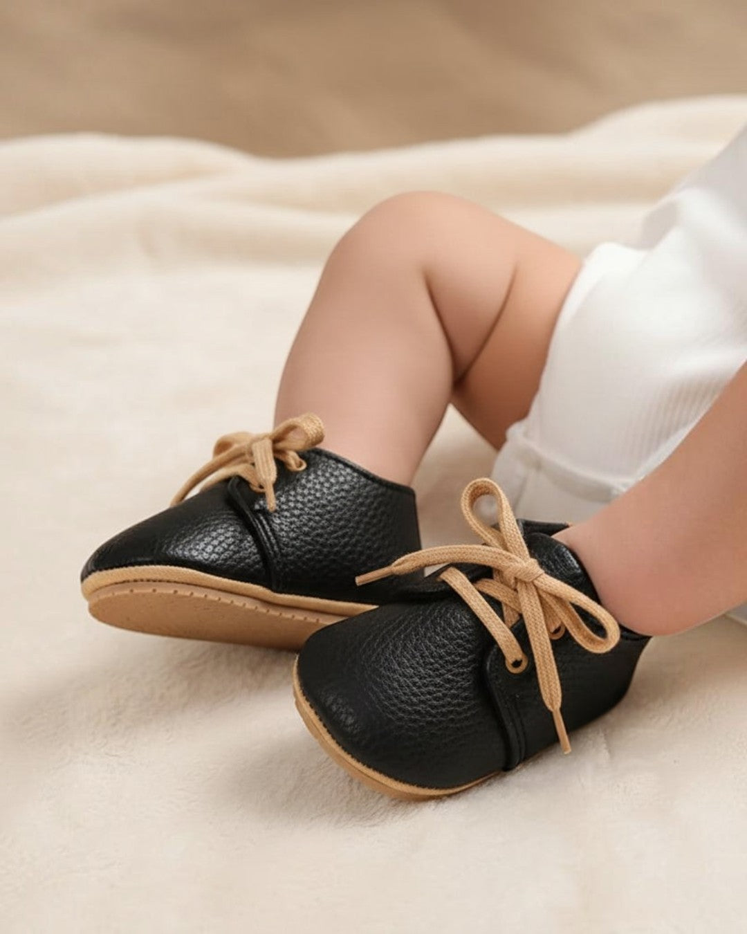 Pair of black baby shoes with tan laces on a white background
