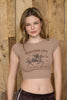 Woman wearing a brown crop top with 'Western Life' design and black shorts against a wooden background
