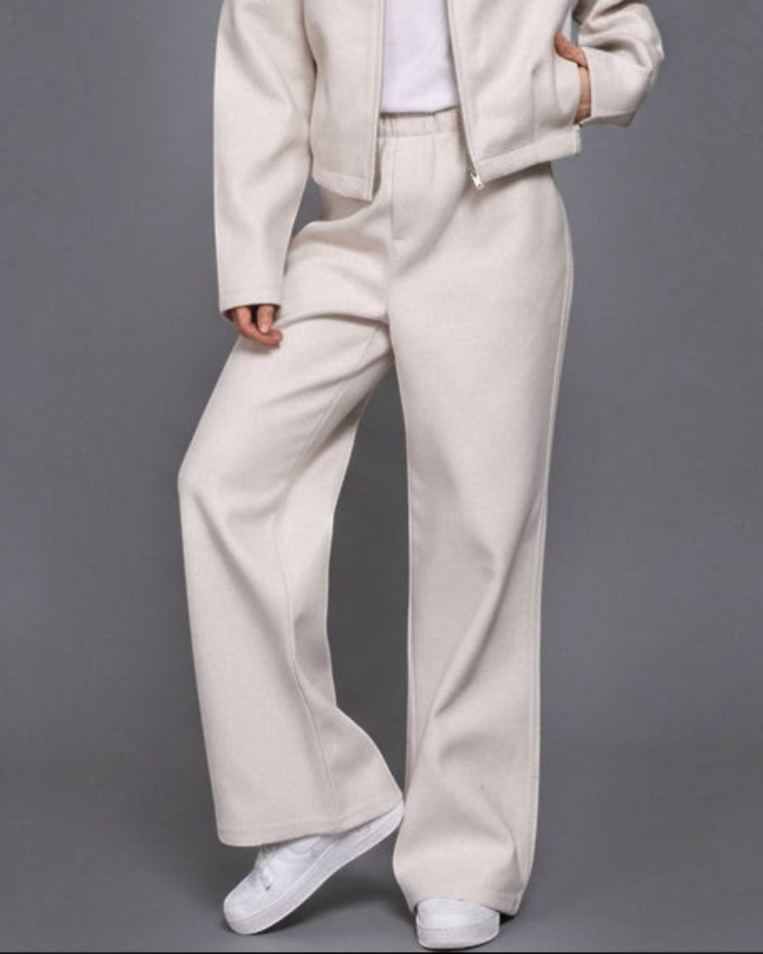Woman wearing a beige jacket and pants set against a gray background
