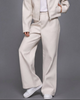 Woman wearing a beige jacket and pants set against a gray background