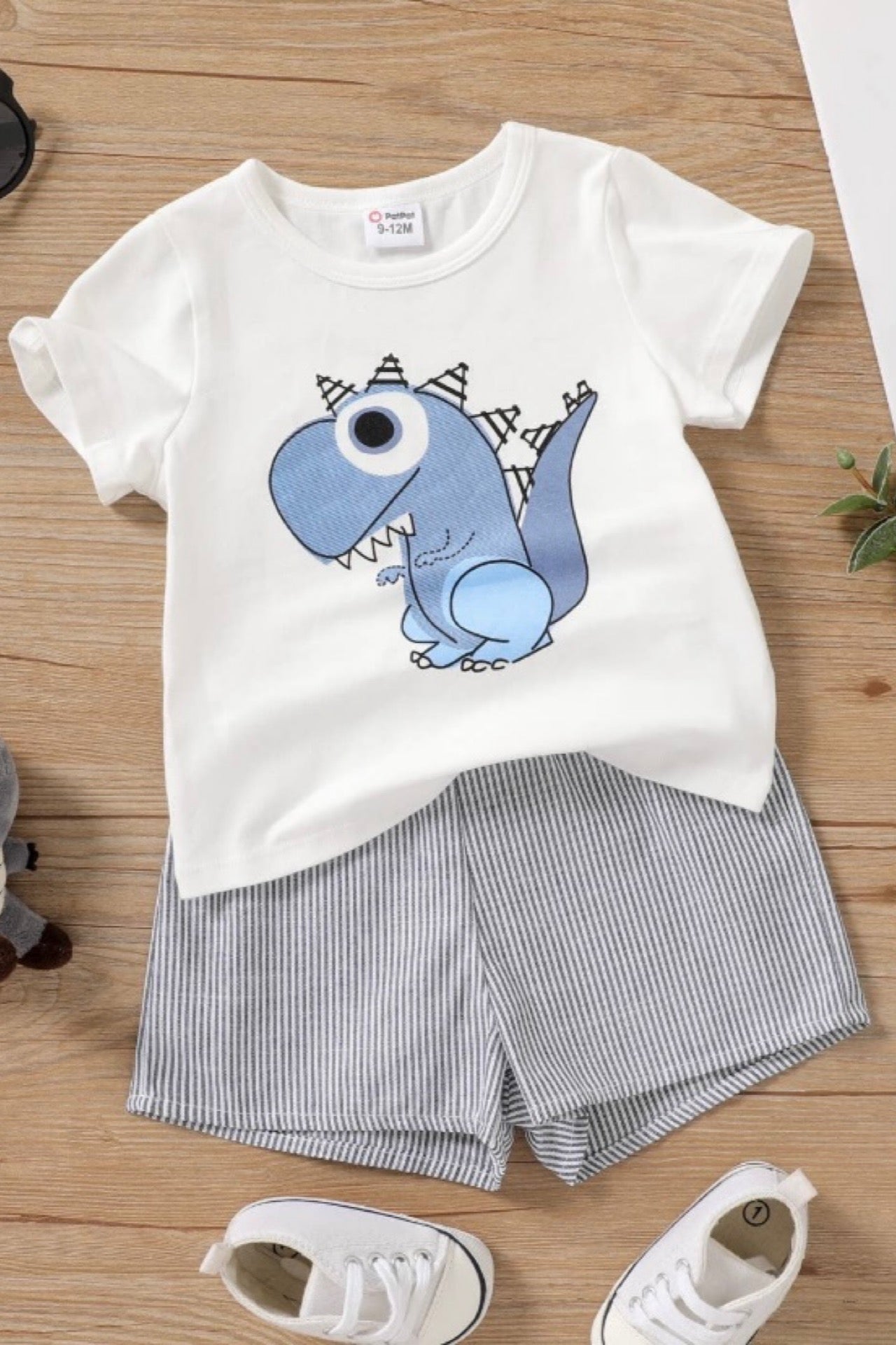 Children's outfit with white t-shirt and striped shorts on a wooden surface, surrounded by accessories.