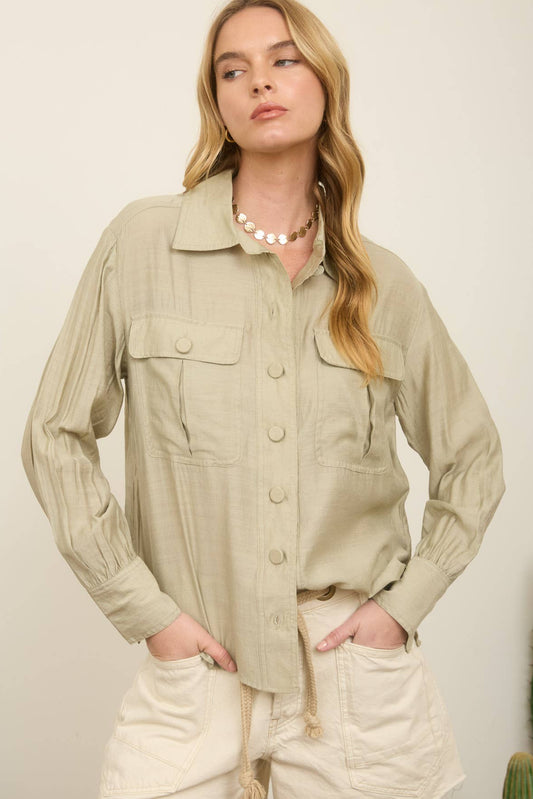 Woman wearing a beige jacket and shorts standing against a plain background with a cactus plant.