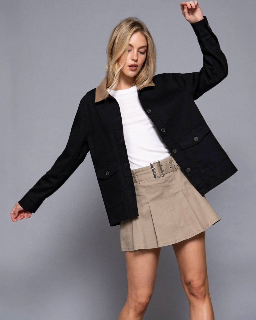 Woman wearing a black jacket, white shirt, and beige skirt on a gray background