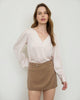 Woman wearing a white blouse with sheer sleeves and a beige skirt against a plain background
