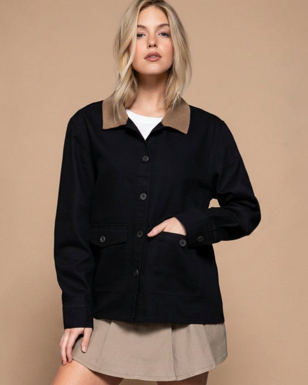Woman wearing a black jacket with a beige collar against a gray background