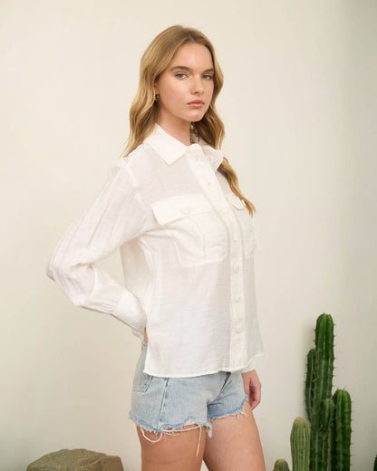 Woman wearing a white shirt and denim shorts standing against a plain background with a cactus plant.