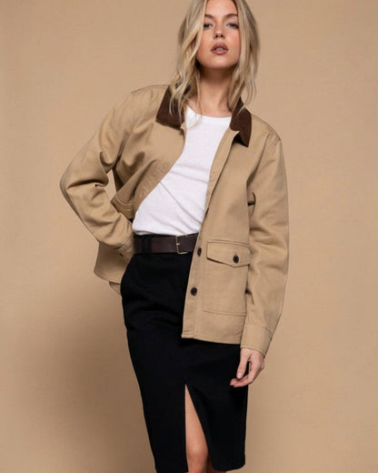 Woman wearing a beige jacket with brown collar and black pants on a gray background