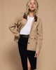 Woman wearing a beige jacket with brown collar and black pants on a gray background
