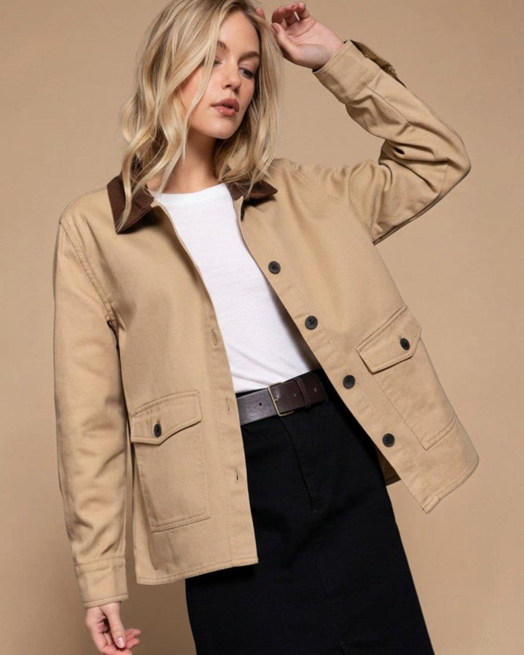 Woman wearing a beige jacket with a white shirt and black pants on a gray background