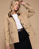 Woman wearing a beige jacket with a white shirt and black pants on a gray background