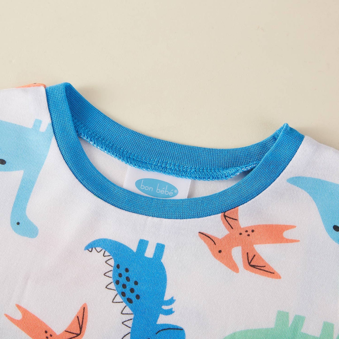 Children's pajama top with dinosaur pattern and blue collar on a beige background