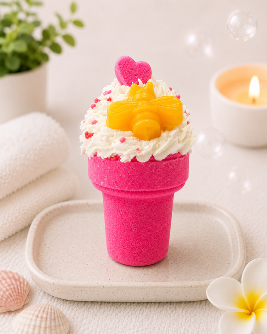 Pink cupcake-shaped candle with white frosting and yellow heart on a white surface with a plant and shell in the background.