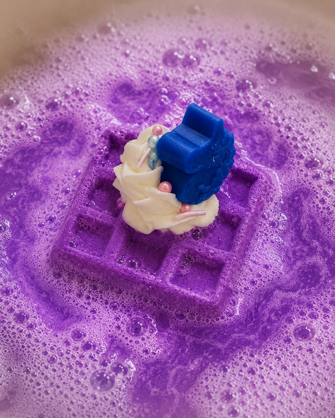 Decorative soap with a bride and groom figure on a purple waffle-shaped soap in soapy water.
