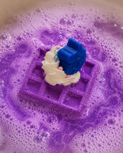 Decorative soap with a bride and groom figure on a purple waffle-shaped soap in soapy water.