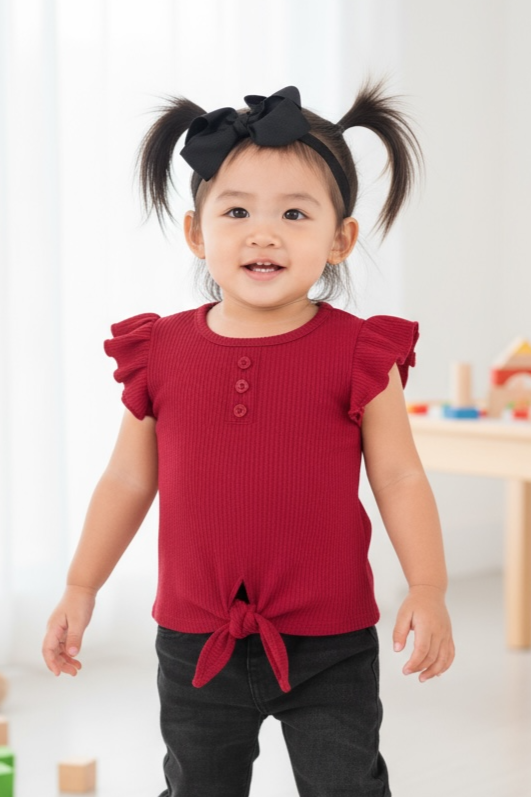 Child wearing a red shirt and black pants standing in a room with toys.