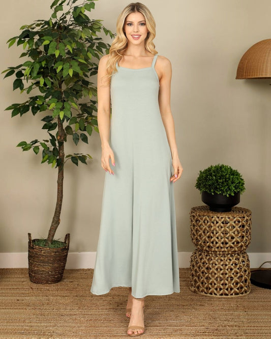 Woman wearing a light blue dress standing in a room with a plant and decorative table.