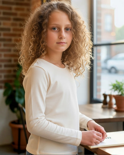 Young girl in a white sweater sitting at a desk with a window and plants in the background