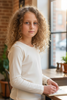 Young girl in a white sweater sitting at a desk with a window and plants in the background
