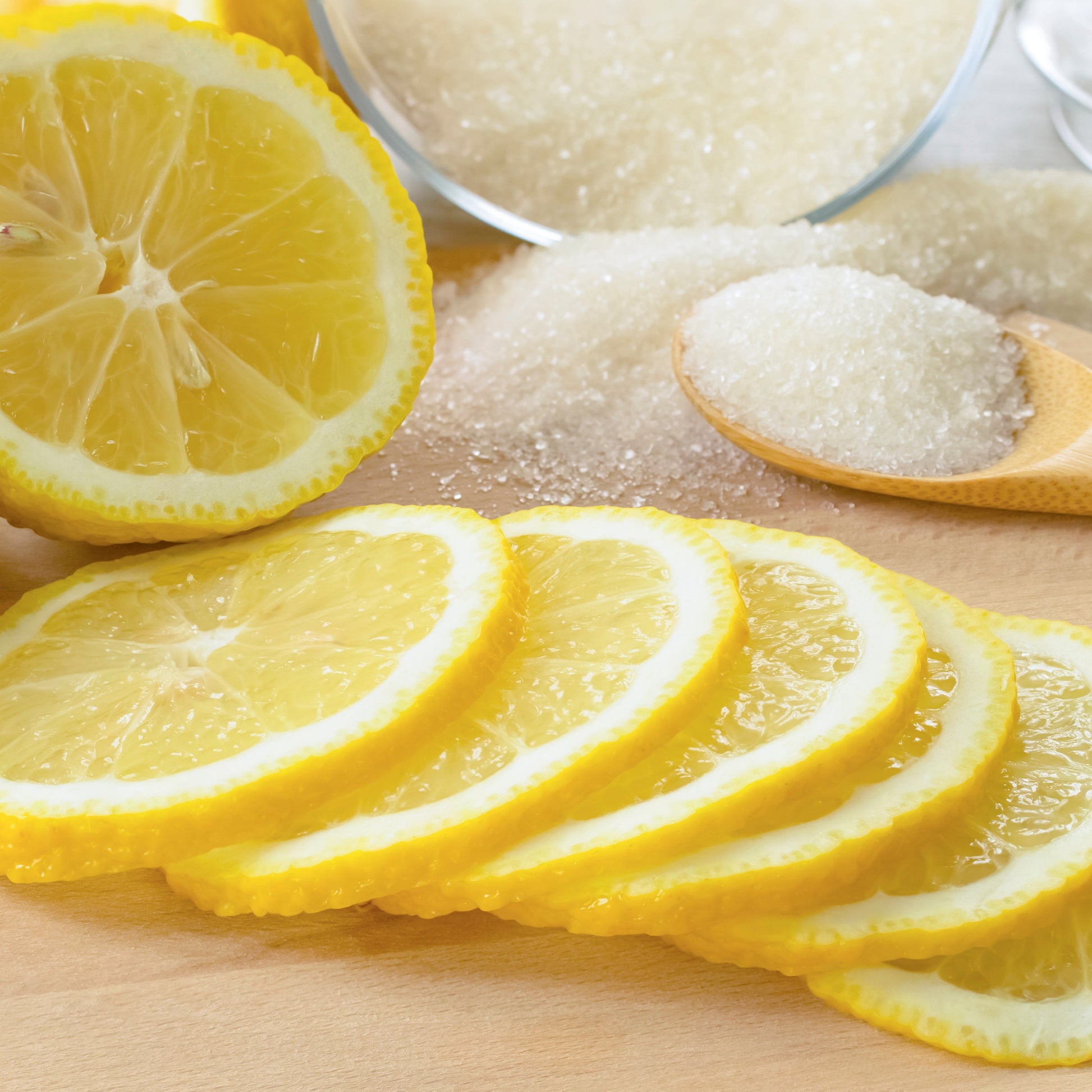 Sliced lemons on a wooden cutting board with a bowl of sugar and a spoon.