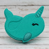 Turquoise narwhal-shaped object on pebbles