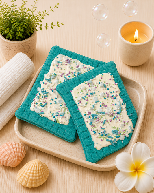 Two decorative coasters with blue borders on a wooden tray, surrounded by a candle, plant, and shells.