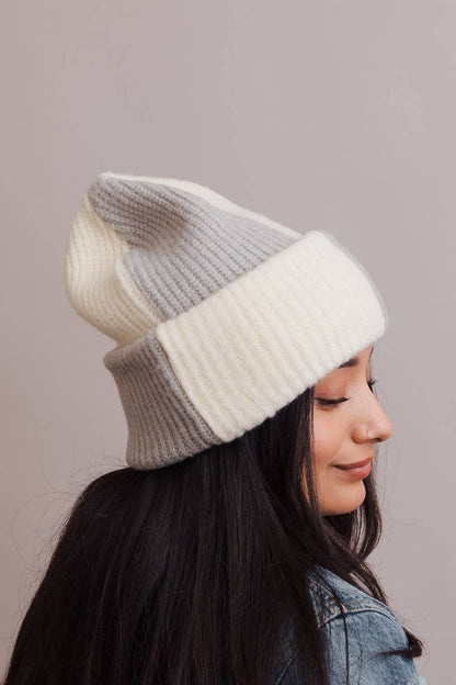 Person wearing a two-tone knit beanie in gray and white on a plain background