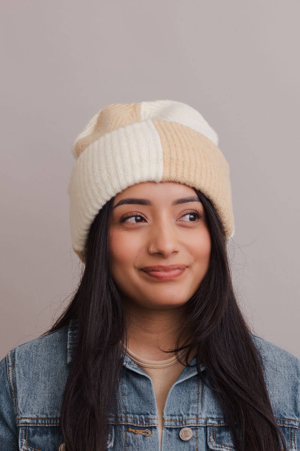 Woman wearing a beige and white striped beanie against a plain background