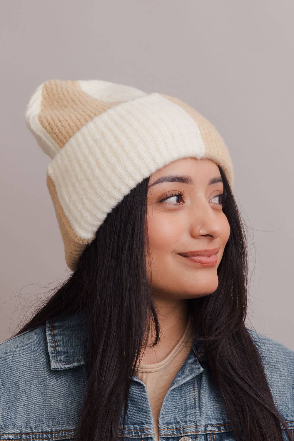 Woman wearing a beige and brown striped knit beanie against a plain background