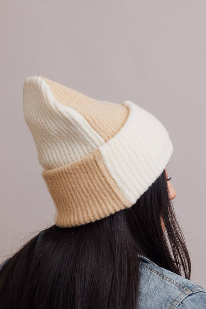 Two-tone beige and white knit beanie worn by a person with a neutral background