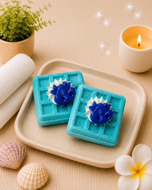 Two blue waffle-shaped soaps with a blue lion figure on a beige plate, surrounded by bubbles, a candle, and decorative items.