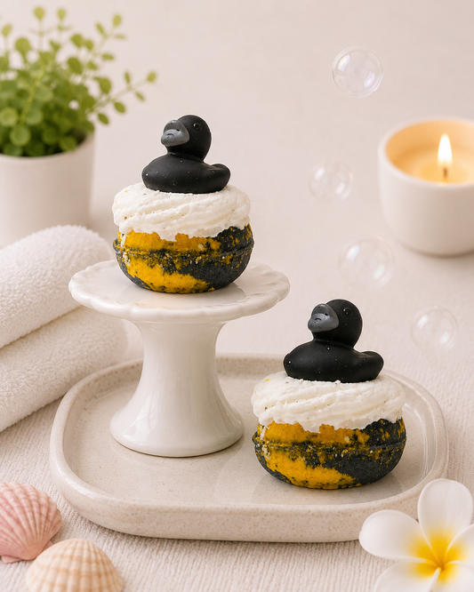 Two small desserts with black duck decorations on a white plate, surrounded by a candle and plants.