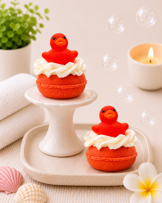 Two red rubber duckies with white frosting on a white stand and surface, surrounded by bubbles and flowers.