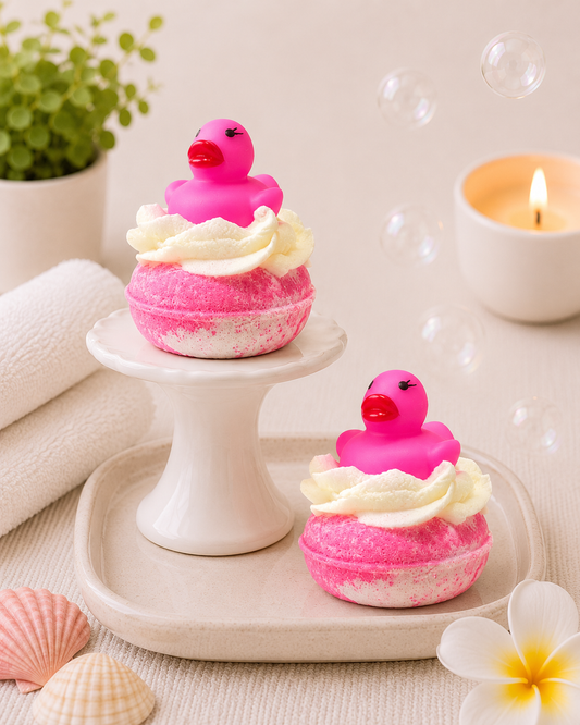 Two pink bath bombs with duck decorations on a white stand and tray, surrounded by bubbles and flowers.