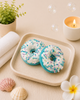 Two blue and white decorated donuts on a plate with a candle, flowers, and shells in the background.