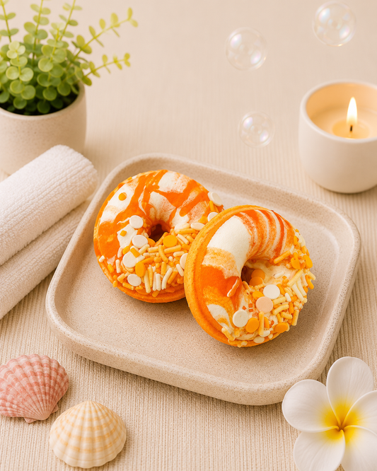 Two decorative donuts on a plate with a candle, shells, and flowers in the background.