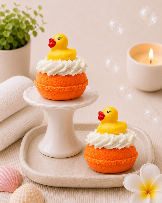 Two orange and yellow rubber duck bath bombs on a white stand with bubbles and flowers in the background.