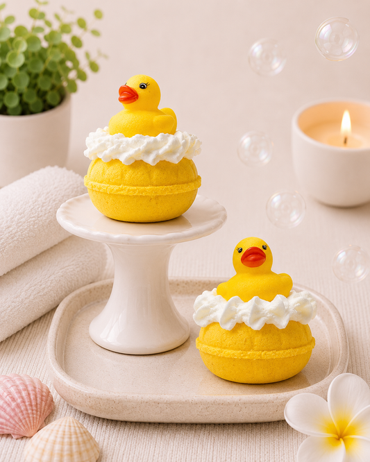Two yellow rubber duck bath bombs with white foam on a decorative stand and surface.