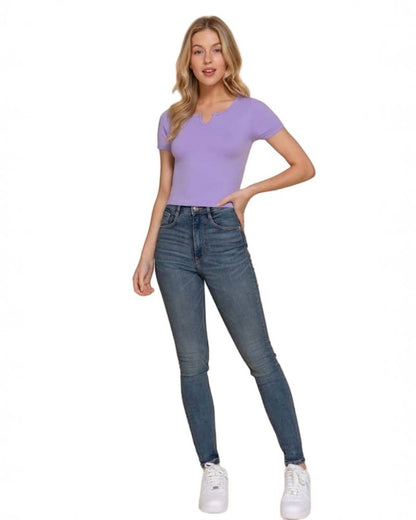 Woman wearing a purple top and blue jeans on a beige background