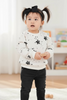 Child wearing a white sweater with black star patterns and black pants in a room.